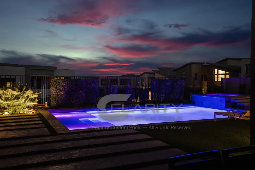 Pool and raised spa glowing with LED lighting after sunset, with stepped deck pads in the foreground