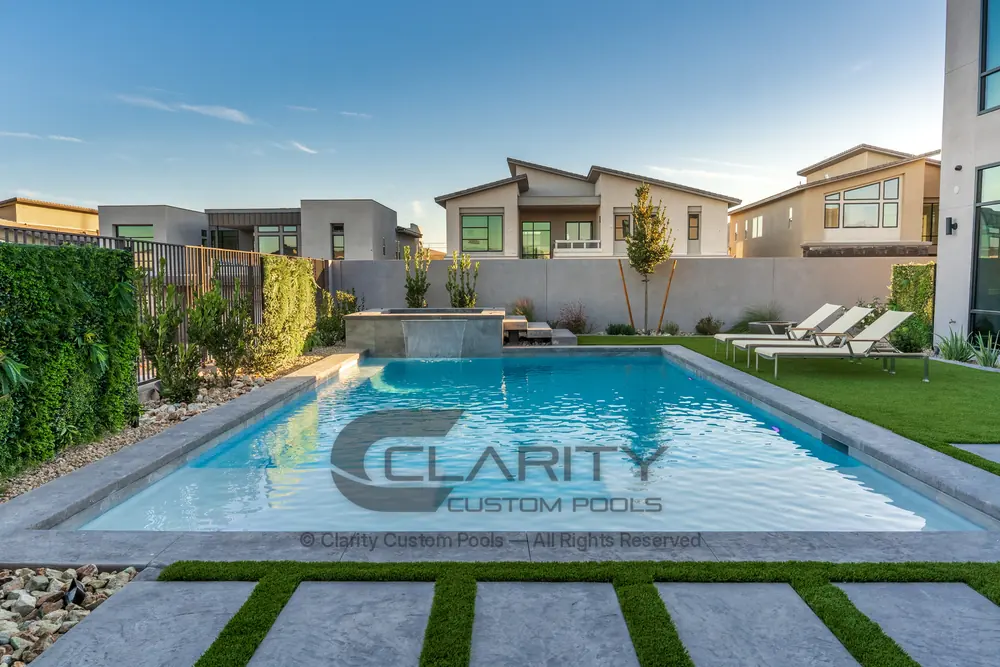 Rectangular pool with a raised spa spillover, concrete coping and paver deck in a walled backyard