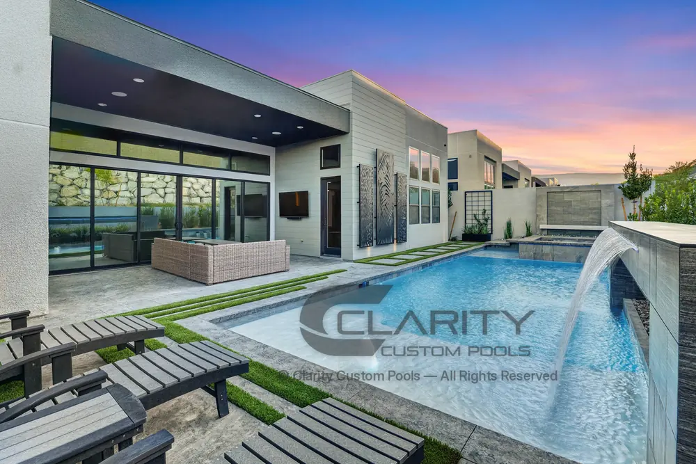Pool at golden hour with a sheer descent from a raised wall, a bubbler on the tanning ledge and loungers on the deck