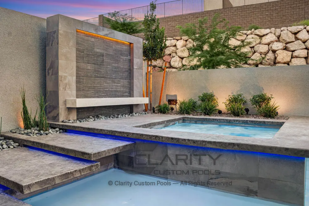 Detail of a raised spa and stone-clad water wall with a sheer descent spilling into the pool
