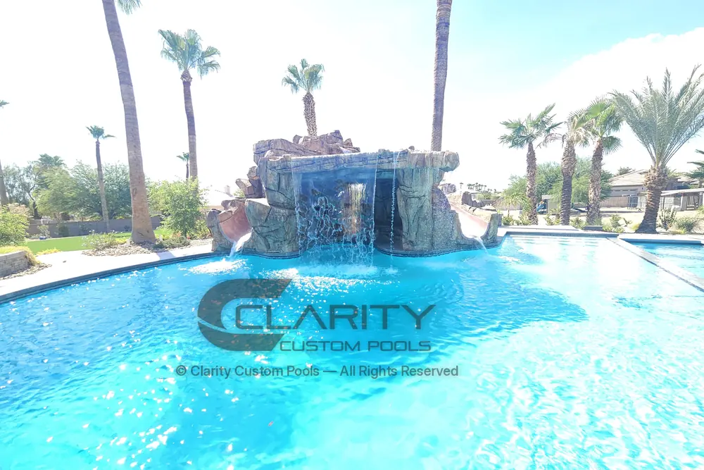 Bright blue freeform pool with a rock grotto waterfall and palm trees against a clear sky