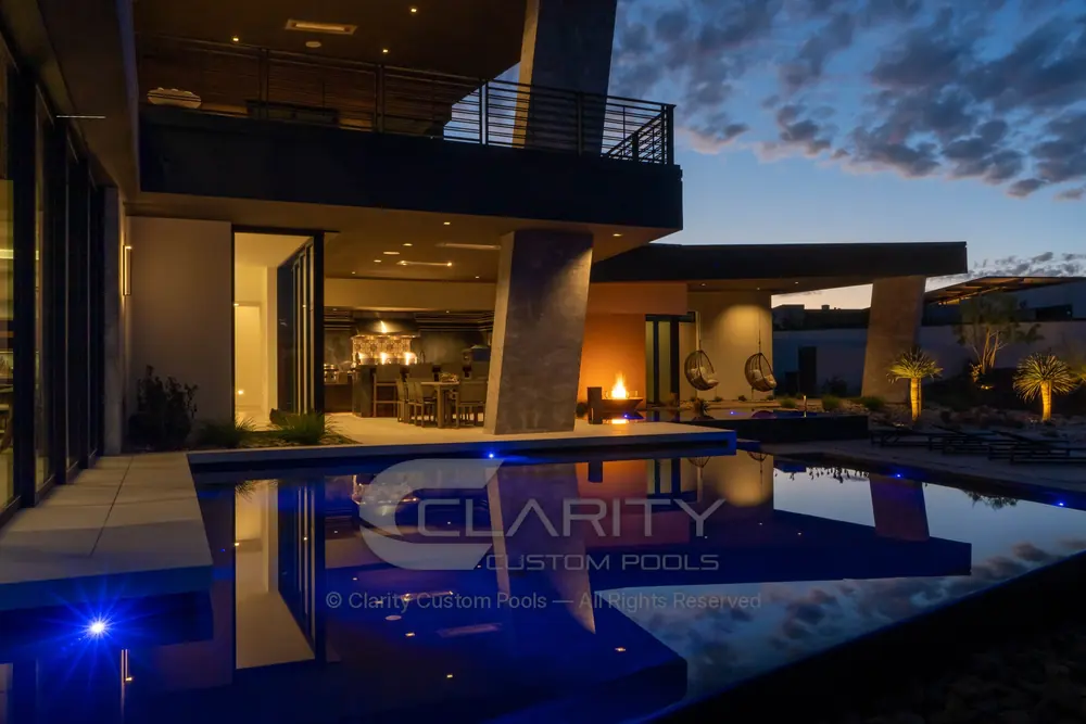 Modern home reflected in a dark pool with blue LED lights at dusk
