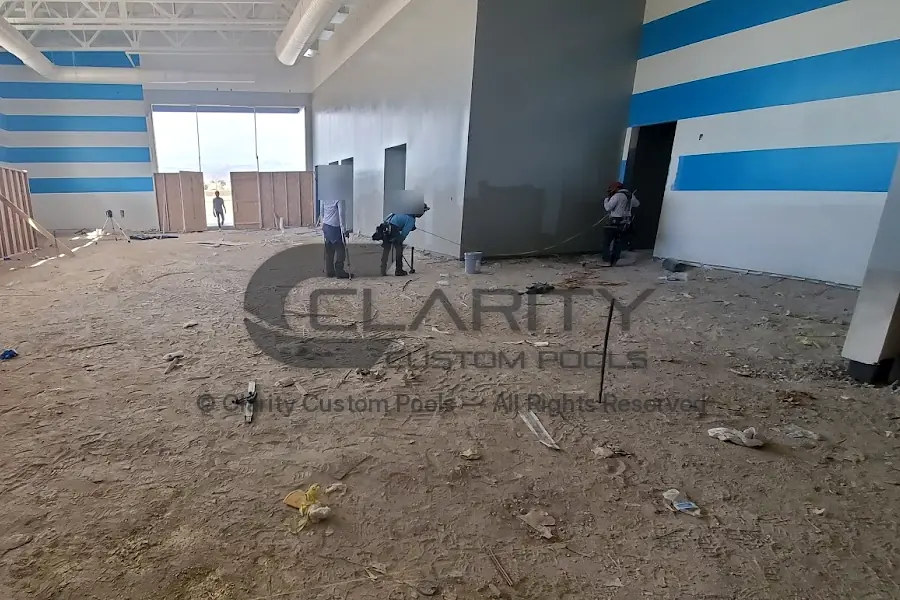 Crew surveying and marking the layout on the dirt floor of an indoor natatorium before excavation