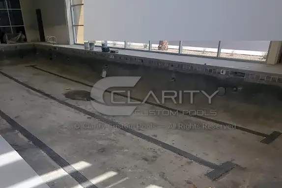 Empty indoor lap pool with dark lane tile lines on the floor and waterline tile installed, before plaster and fill
