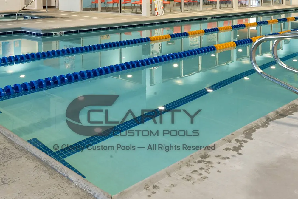 Finished indoor commercial lap pool with blue lane tile, lane lines and a stainless handrail